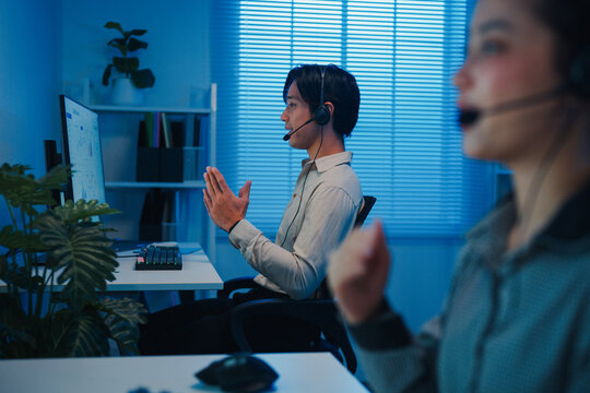 Gen z Asia young call center team or customer support service executive use computer and microphone headset work technical e commerce support in late night office. Telemarketing or sales job concept.