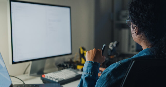 Young African American female programmer coding AI software on multiple screens in night office. Network security, cybersecurity, machine learning, working late, overtime, robotics automation concept.