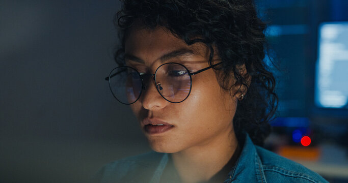Close-up Black female programmer with code reflection in glasses working late in home office at night. Cybersecurity, AI algorithm, Network security, software developer, serious face, burnout concept.