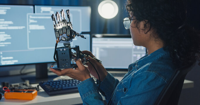 Young African American female programmer coding AI software on multiple screens in night office. Network security, cybersecurity, machine learning, working late, overtime, robotics automation concept.