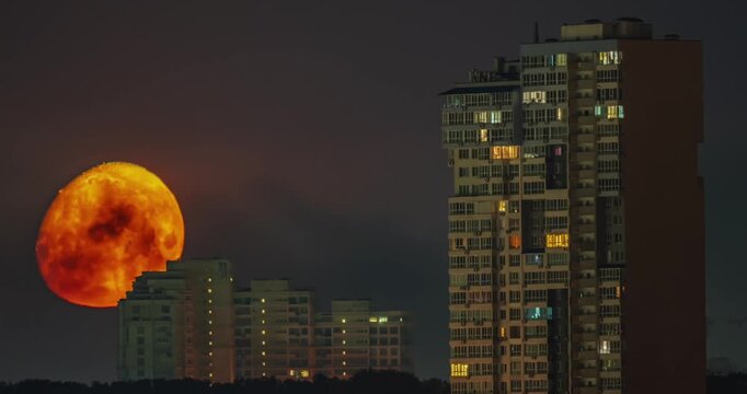 Massive orange full moon setting behind city skyscrapers at night time lapse
