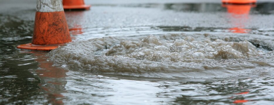 Traffic cone standing in flooded water on paved street