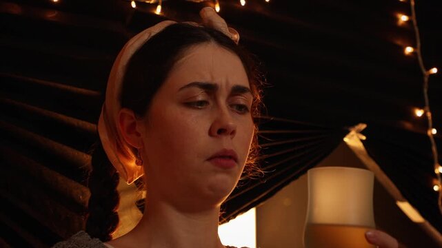 Portrait of a young Caucasian woman relaxing at home in the evening, smelling wine in a glass with a doubtful expression. Wine tasting, disappointment, leisure, and everyday lifestyle concept.