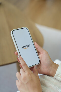 Amazon logo on a smartphone screen in a dark room and a finger pointing at it