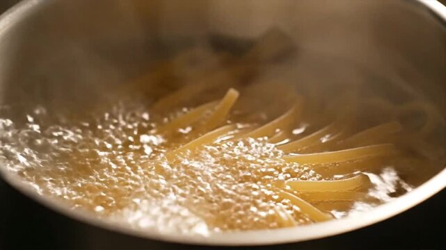 Close up macro shot of long pasta noodles swirling in vigorously boiling water with rising steam
