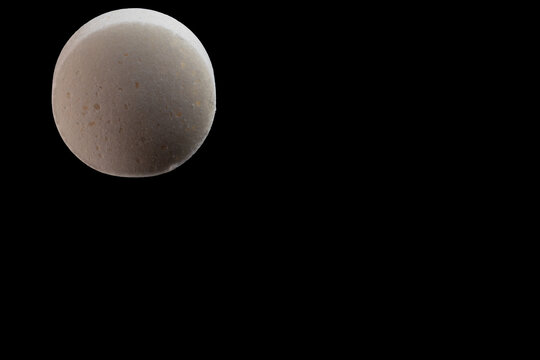 High-resolution closeup of single glucose and salt tablet with copy space on black background, isolated macro extreme detail v1