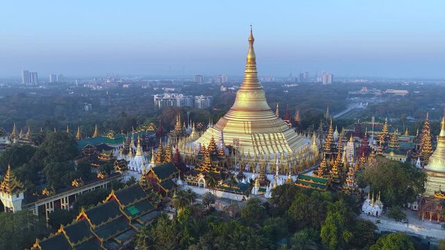 Aerial drone view at Shwedagon Pagoda, a golden stupa, surrounded by lush greenery and urban development in Yangon (Rangun), Myanmar (Burma), showcasing the city's blend of religious and modern life.