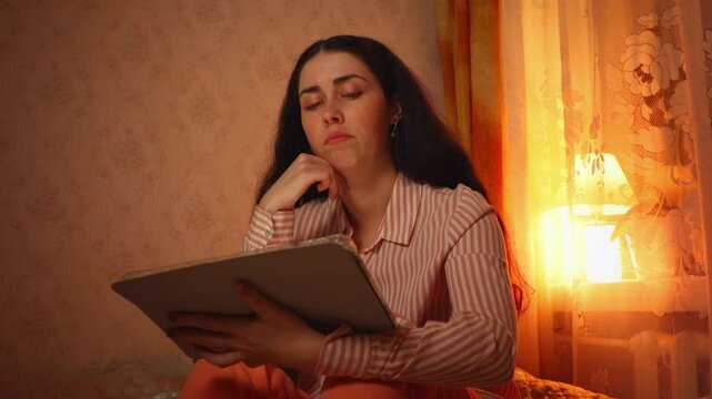 Mid shot portrait of a beautiful thoughtful young Caucasian woman with braces smiling softly while watching an online stream in the evening. Digital entertainment, home relaxation, and modern lifestyl