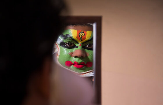Kathakali dancer looking in the mirror during the final stages of makeup.
