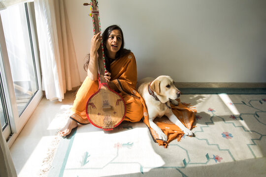 Woman sitting with her dog by her side and playing music on her tambura. 