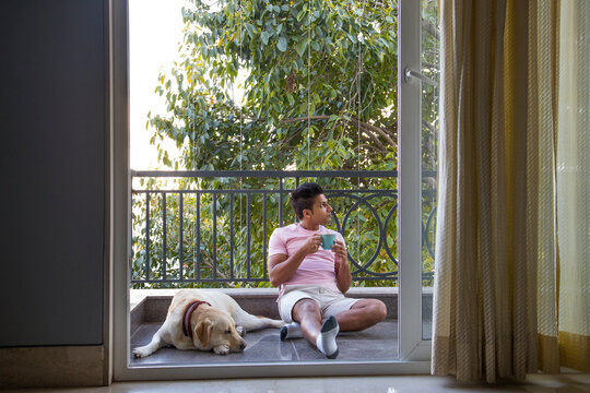 Man drinking coffee and spending some quality time with his dog in the balcony. 