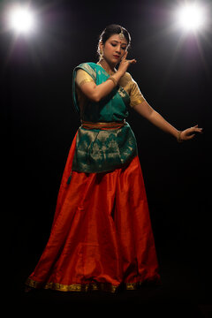 Kathak dancer giving a mesmerising performing in front of a dark background. 