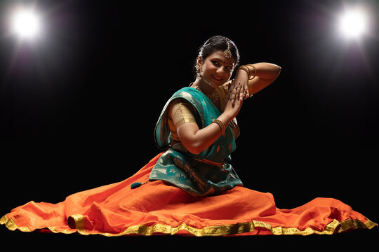 Kathak dancer sitting gracefully in front of a dark background. 