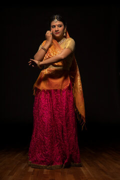 Kathak dancer giving a mesmerising performing in front of a dark background. 