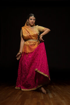 Kathak dancer giving a mesmerising performing in front of a dark background. 