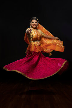 Kathak dancer circling gracefully during a performance in front of a dark background. 
