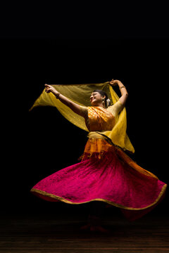 Kathak dancer circling gracefully during a performance in front of a dark background. 