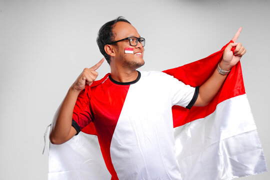 Smiling young Asian man is holding country flag and pointing to the copy space beside him.