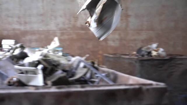 Machine claw crushing a scrapped white appliance flat against a steel press bed inside a recycling plant