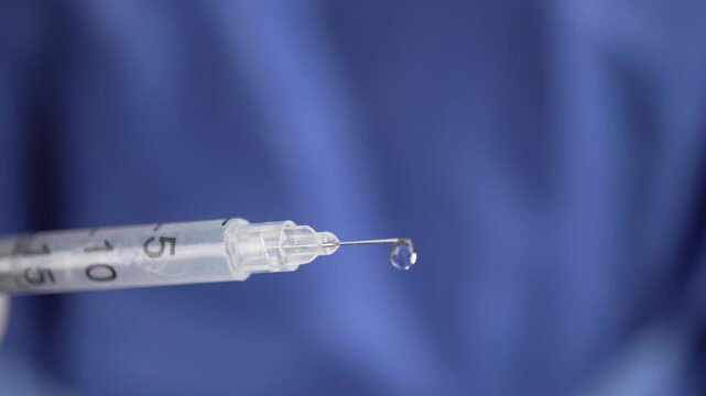 Close-up of an insulin syringe needle forming a clear droplet against a blue medical backdrop, useful for health care, vaccination, or diabetes treatment concepts.
