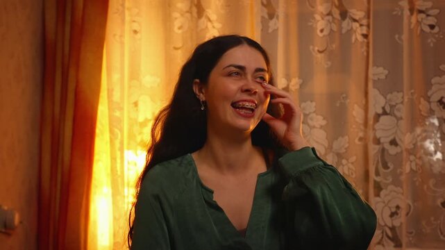 Portrait of a beautiful young Caucasian woman with braces laughing happily while sitting on a bed in an evening room. Positive emotions, joyful lifestyle, self confidence, and cozy home atmosphere con