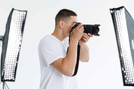 Side view of young man photographer taking photo using professional dslr camera and lighting equipment