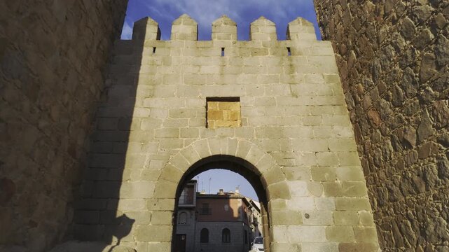 Handheld footage captures the iconic medieval &Aacute;vila castle walls at golden hour, showcasing ancient stonework, battlements, and a dramatic arched gate under a vivid sunset sky. No people visible.