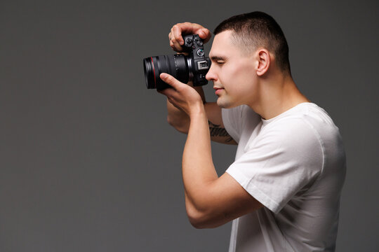 Young male photographer with camera in professionally equipped on gray background