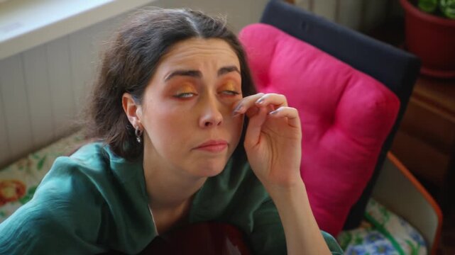 Top view of a tired young Caucasian woman yawning while sitting on a bed. Boredom, loneliness, fatigue, and emotional exhaustion concept in a cozy home atmosphere