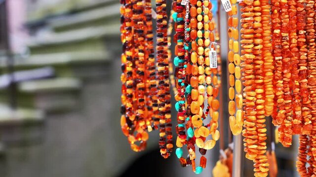 Amber jewelry displayed in outdoor market showcase in Gdansk, Poland. Assorted necklaces bracelets earrings pendants and rings featuring polished Baltic amber are arranged for sale display case. Warm