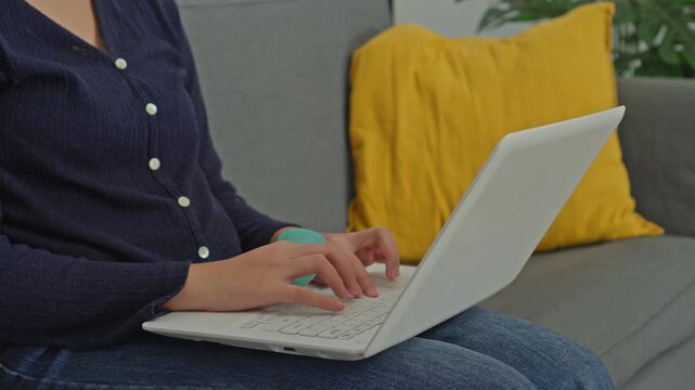 Woman browsing internet on laptop computer while holding green silicone menstrual cup.