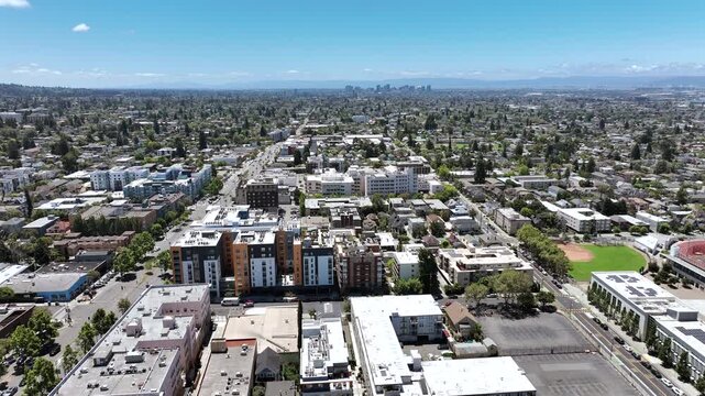 Smooth aerial drone footage descending toward a residential neighborhood near downtown Berkeley, California, featuring apartment buildings, tree-lined streets, surrounding homes, and the dense urban