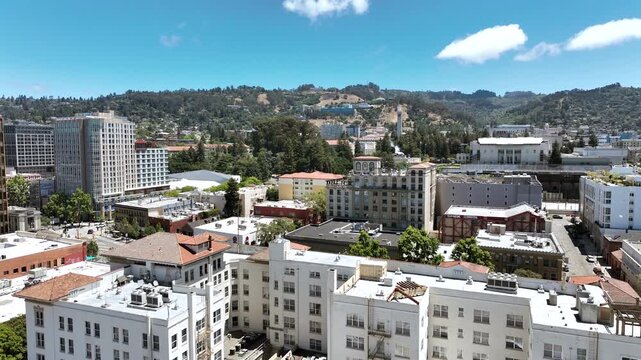 Smooth ascending drone footage over downtown Berkeley, California, revealing urban buildings, tree-lined residential neighborhoods, city streets, and the rolling East Bay hills in the distance.