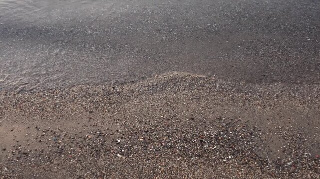 Top view of gentle ocean sea waves washing across wet sandy beach, creating natural shoreline patterns and textured surface. Minimal coastal landscape with moving water soft foam earthy sand tones and