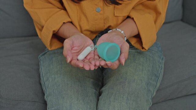 Reusable menstrual cup and white cotton tampon held in hands for feminine hygiene choice concept