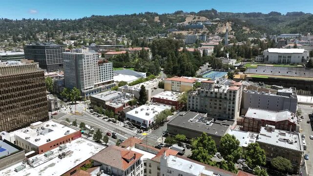 Panoramic drone view over Berkeley, California, featuring the downtown district, dense green neighborhoods, high-rise buildings, the surrounding university district, and scenic East Bay hills beneath