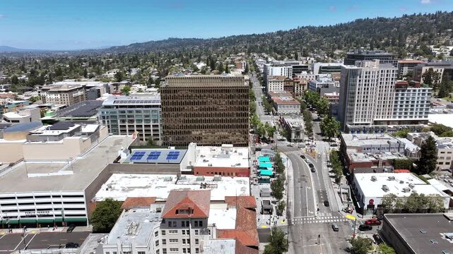 Cinematic leftward drone movement over Berkeley, California, featuring downtown towers, apartment buildings, tree-lined urban neighborhoods, and a scenic mountain range in the background on a bright