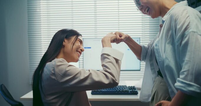 Young Asian businesswomen team doing fist bump on desk at office. Corporate teamwork success celebration, professional colleague partner support, happy employee project achievement win concept.
