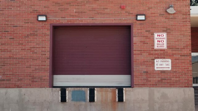 Static shot of a brick loading dock with a closed roll-up door and signs.