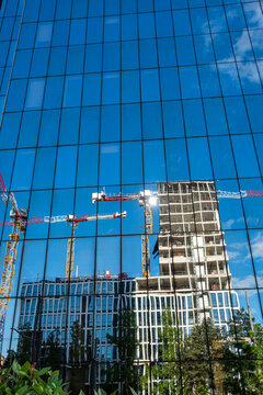 Construction cranes and a rising building appear in reflection across a blue glass facade in Lyon, France, merging sky and architecture into a layered urban scene