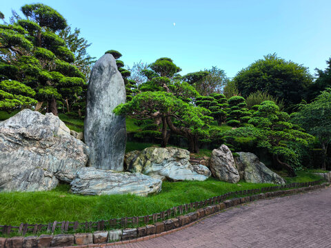 The traditional Chinese green garden landscape features manicured trees and volcanic rock formations at nightfall