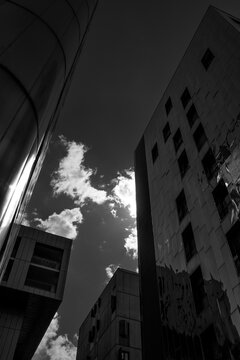 Monochrome buildings frame a bright sky over La Confluence, Lyon, France, where clouds and deep contrast sharpen the upward perspective of contemporary architecture