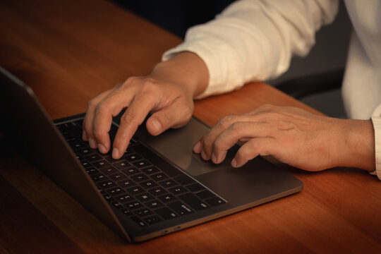 Close up view of professional business man hands typing on laptop computer keyboard while working at wooden office desk using internet technology for digital communication and work.