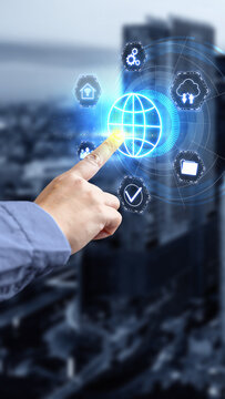 Hand of a businessman touching a futuristic virtual interface with a global network globe icon and technology icons, with a blurred modern city in the background. Concept of Remote working