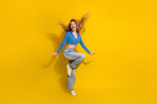 Joyful young woman with long blonde curls jumps playfully against a vibrant yellow background showing a dynamic pose