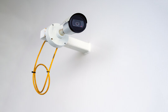 Konzept Security: Seitenansicht auf eine an eine wei&szlig;e Wand montierte Sicherheitskamera oder &Uuml;berwachungskamera im Au&szlig;enbereich mit viel Copy Space, selektive Sch&auml;rfe