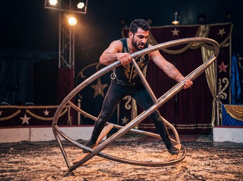 Muskul&ouml;ser m&auml;nnlicher Zirkusartist steht halbnah im Rh&ouml;nrad und dreht sich unter Scheinwerferlicht in der Manege