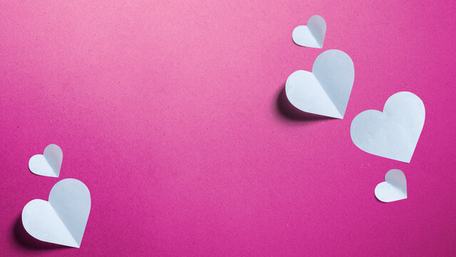 Minimalist concept of love and relationship featuring black paper cutouts of a man and a woman with a white folded paper heart on a textured pink background. Concept of First Love Day