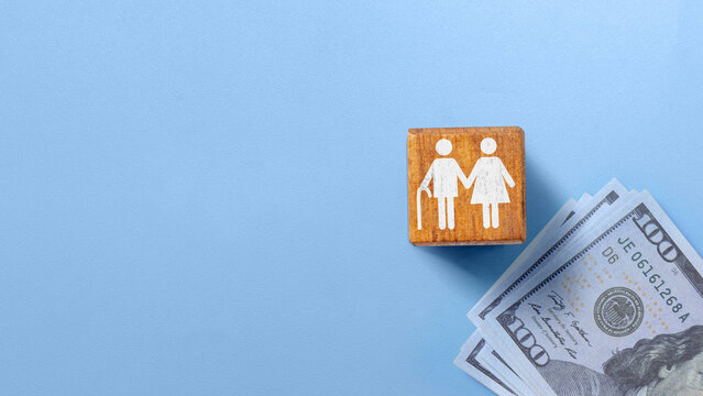 Wooden block with senior couple icon next to US dollar bills on a blue background, symbolizing retirement planning and pension savings. Concept of Pension