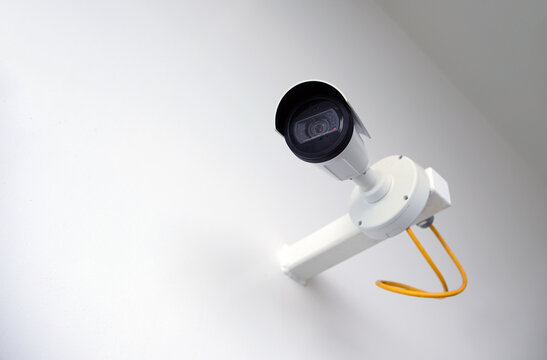 Konzept Security: Seitenansicht auf eine an eine wei&szlig;e Wand montierte Sicherheitskamera oder &Uuml;berwachungskamera im Au&szlig;enbereich mit viel Copy Space, selektive Sch&auml;rfe